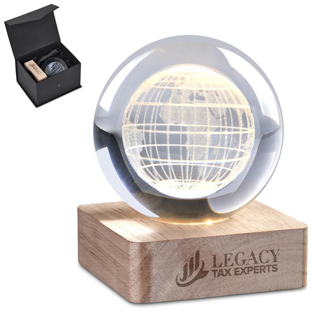 A clear glass globe lamp glowing with warm light, resting on a rectangular wooden base engraved with the Legacy Tax Experts logo. A small black presentation box is shown in the upper left corner on a white background.