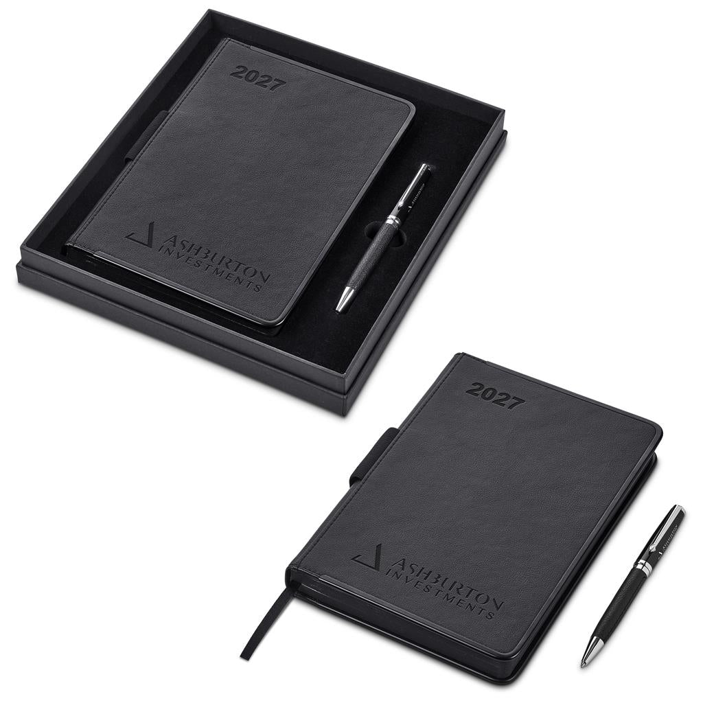 A black 2027 planner set by Ashton Investments, shown both inside its open presentation box and as a standalone item. The set includes a black textured leather cover with the Ashton Investments logo and '2027' printed on the top, accompanied by a matching black pen with a silver clip.