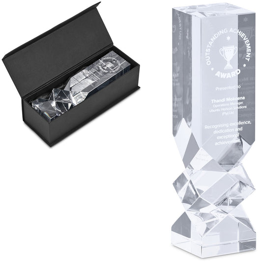 A clear acrylic award trophy with a faceted geometric base, shown next to its open black presentation box containing a matching engraved card.

