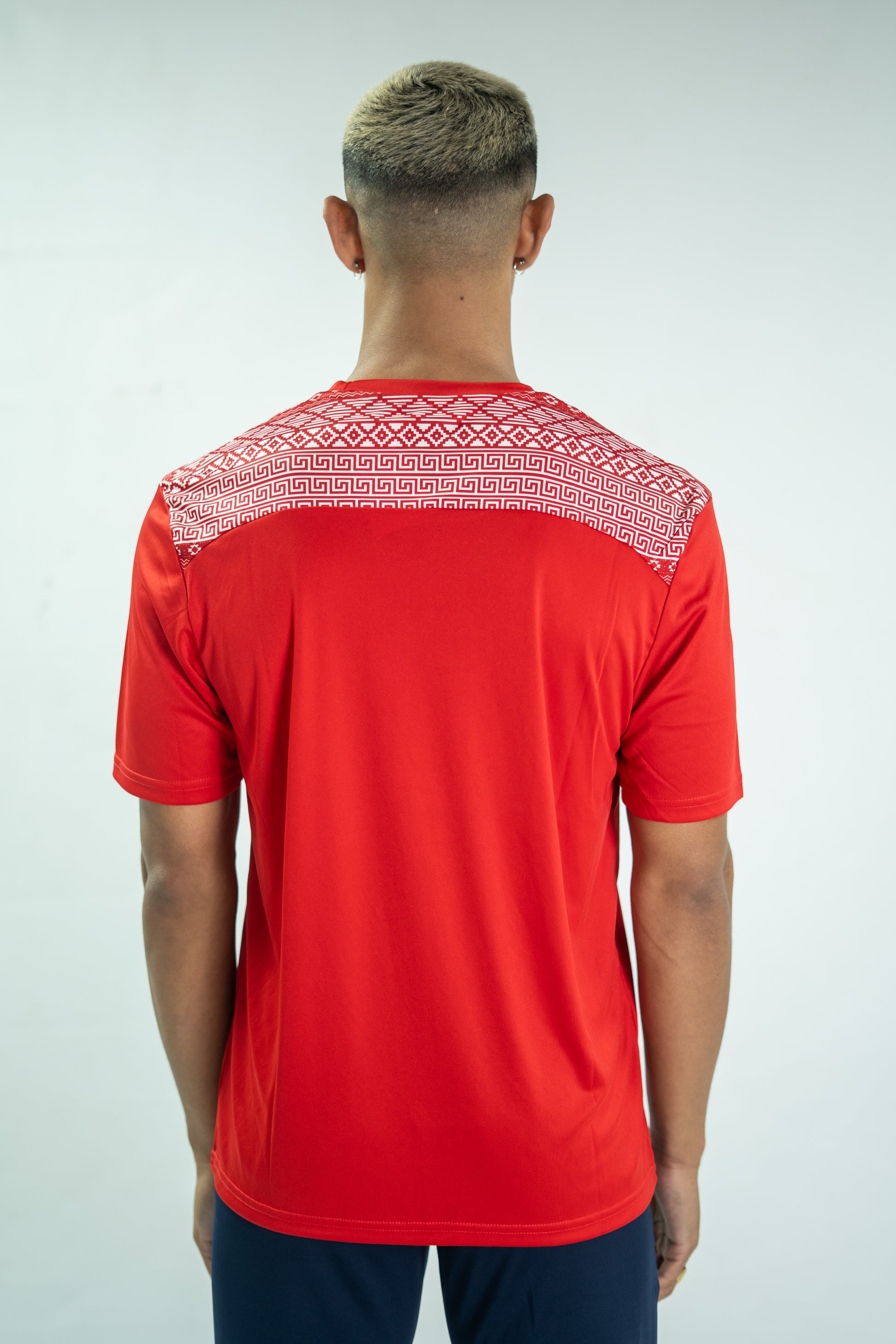 Person wearing a red shirt with white pattern on the back against a light gray background
