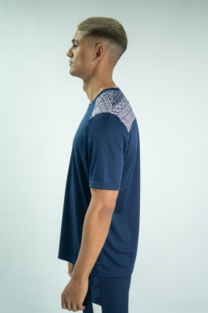 Person wearing a blue t-shirt with patterned shoulder area on a light gray background

