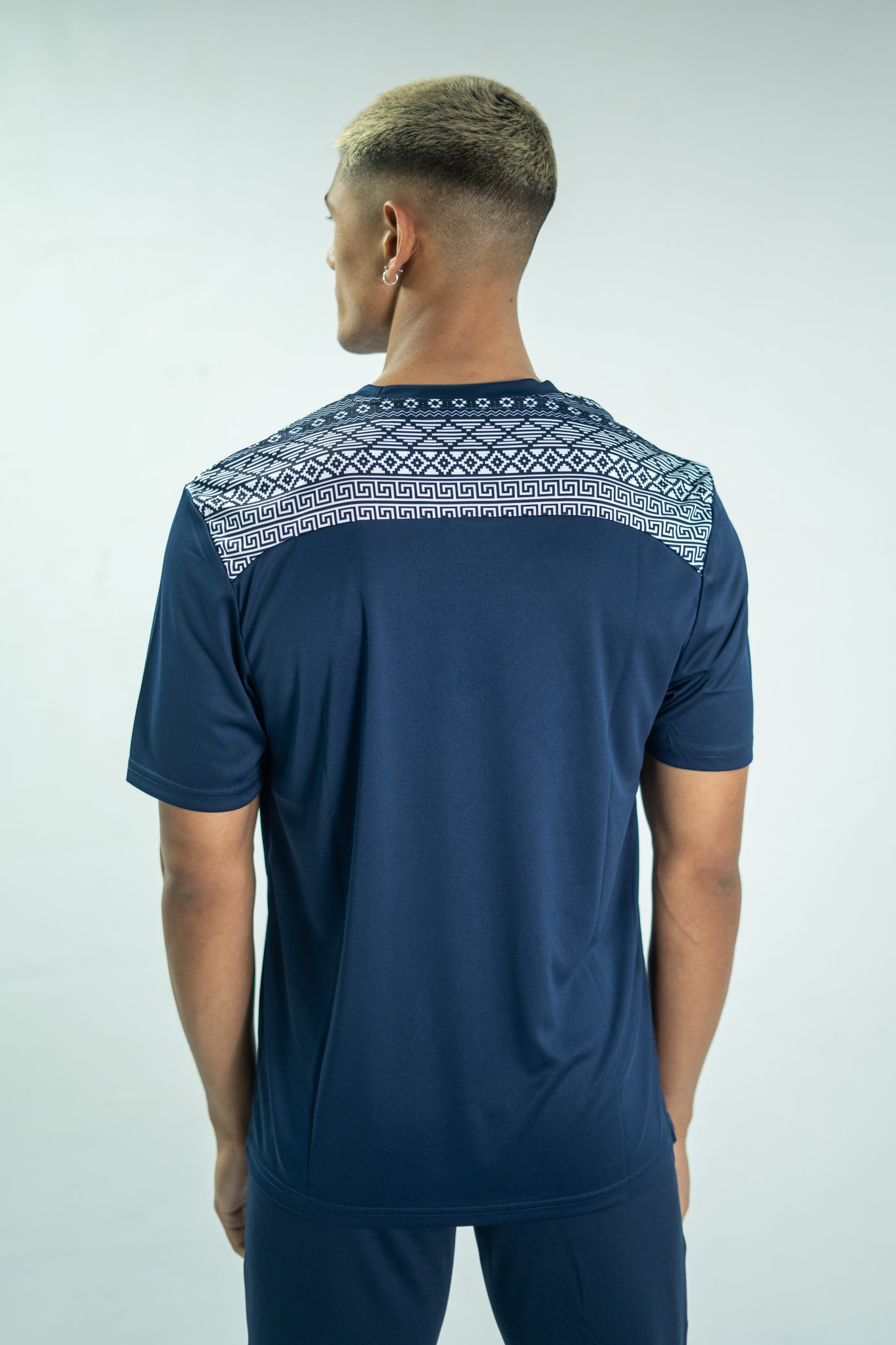 Man wearing a navy blue t-shirt with a patterned shoulder design on a light gray background

