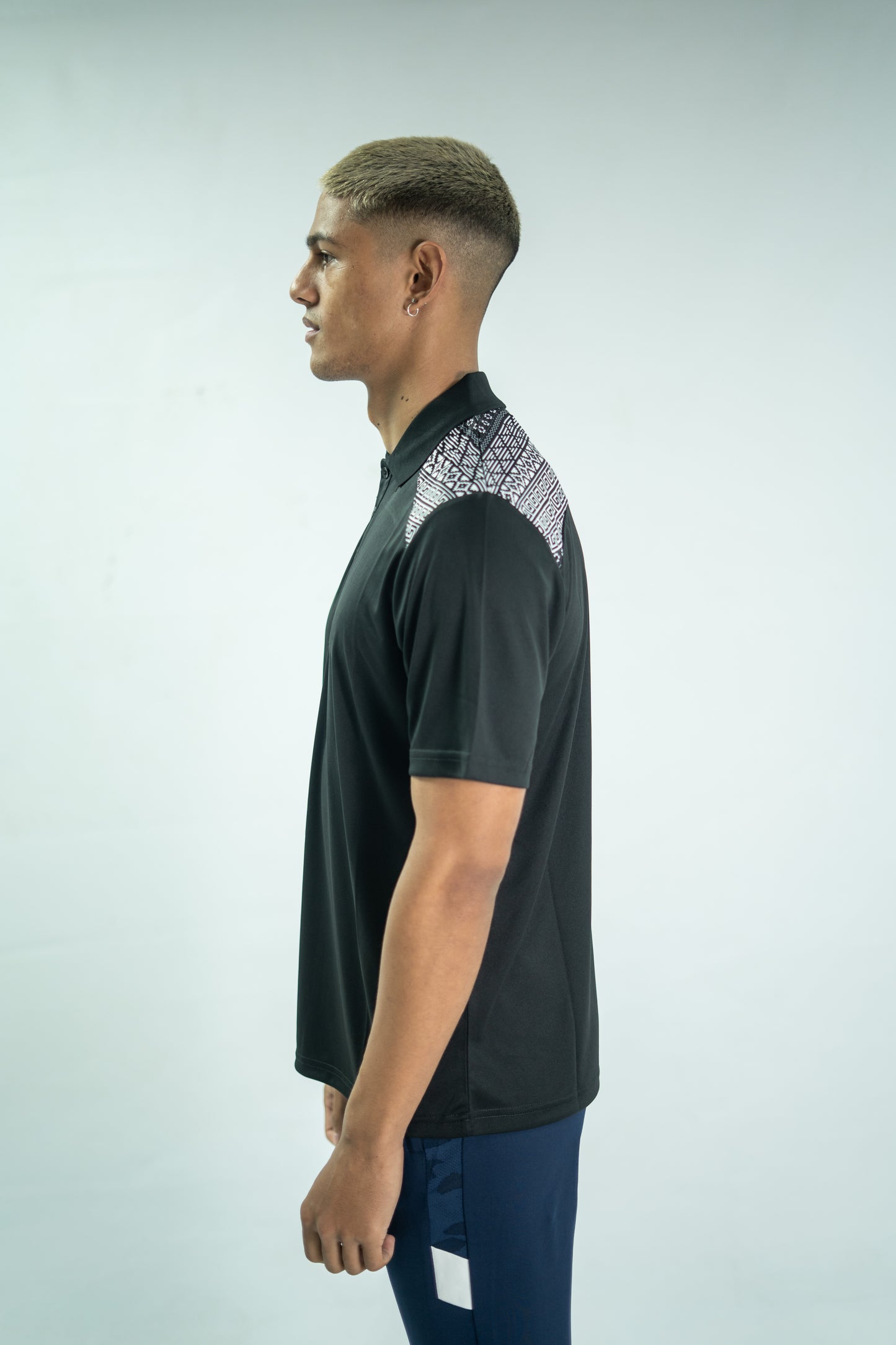 Man wearing a black polo shirt with geometric pattern on a light gray background

