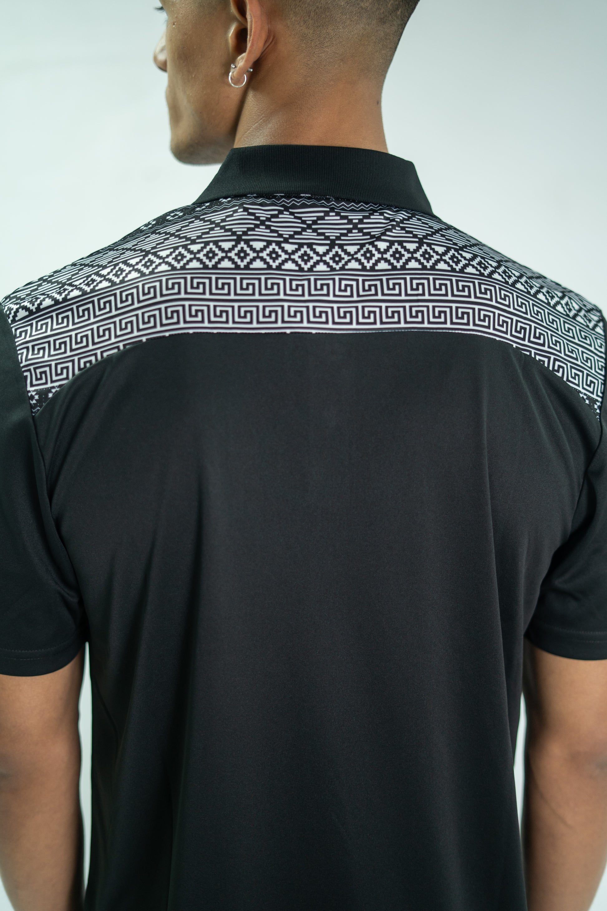 Black shirt with geometric pattern on collar worn by a person against a white background

