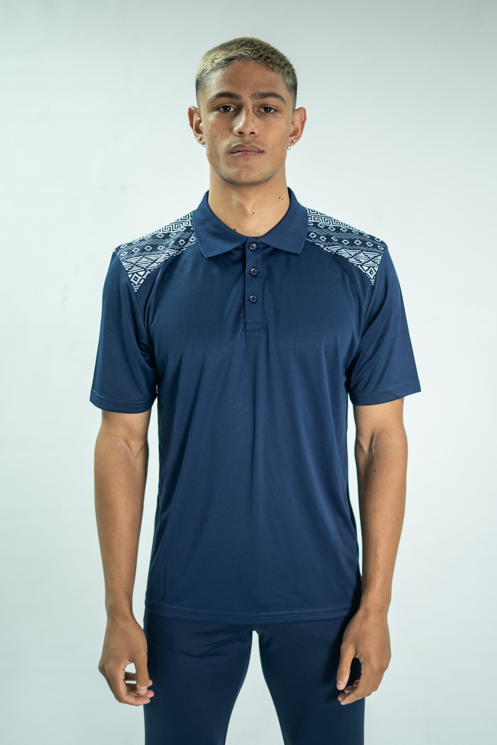 Man wearing a blue Adidas polo shirt with patterned shoulders on a white background

