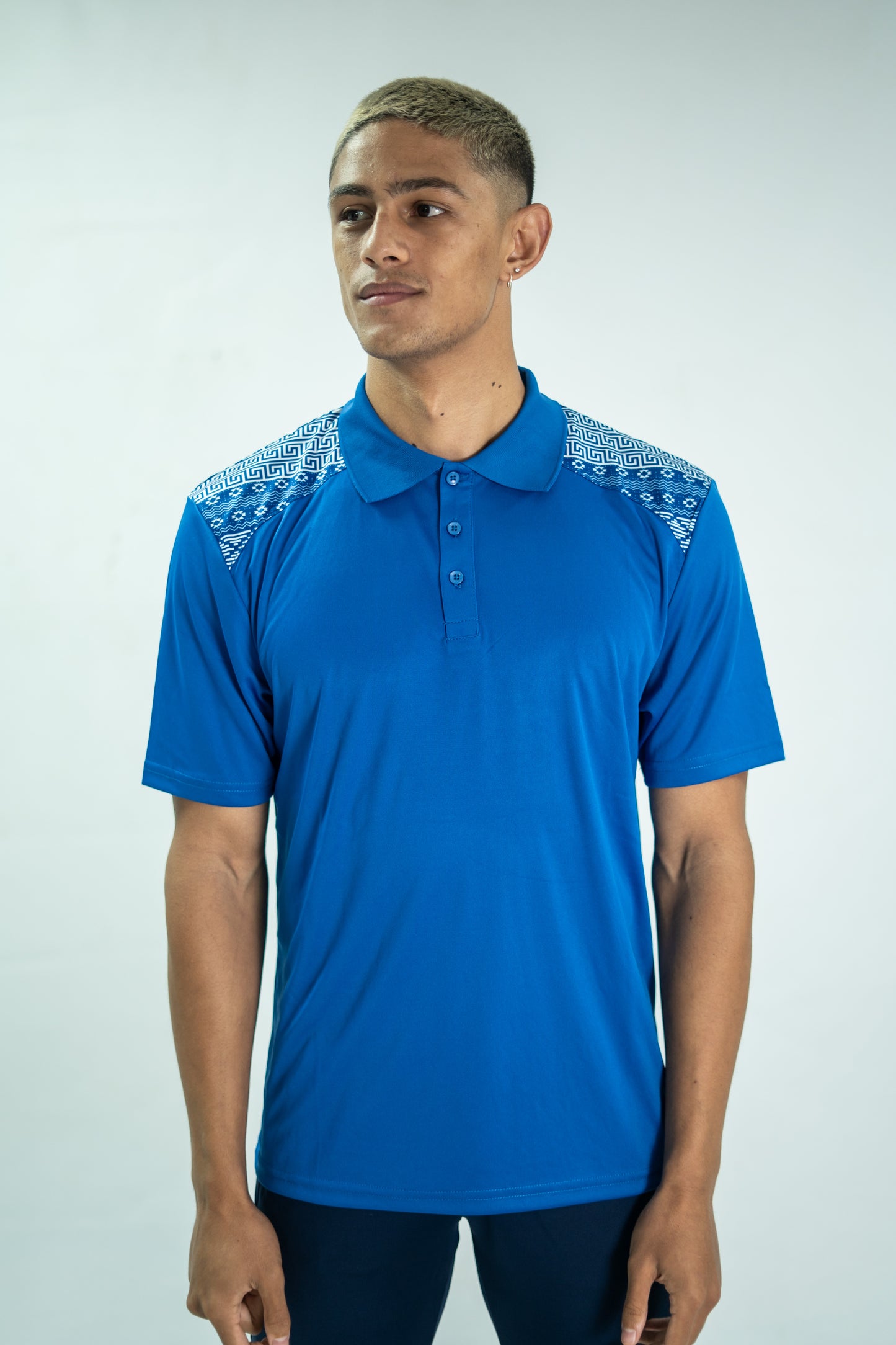 Person wearing a blue polo shirt with white patterns on a plain background

