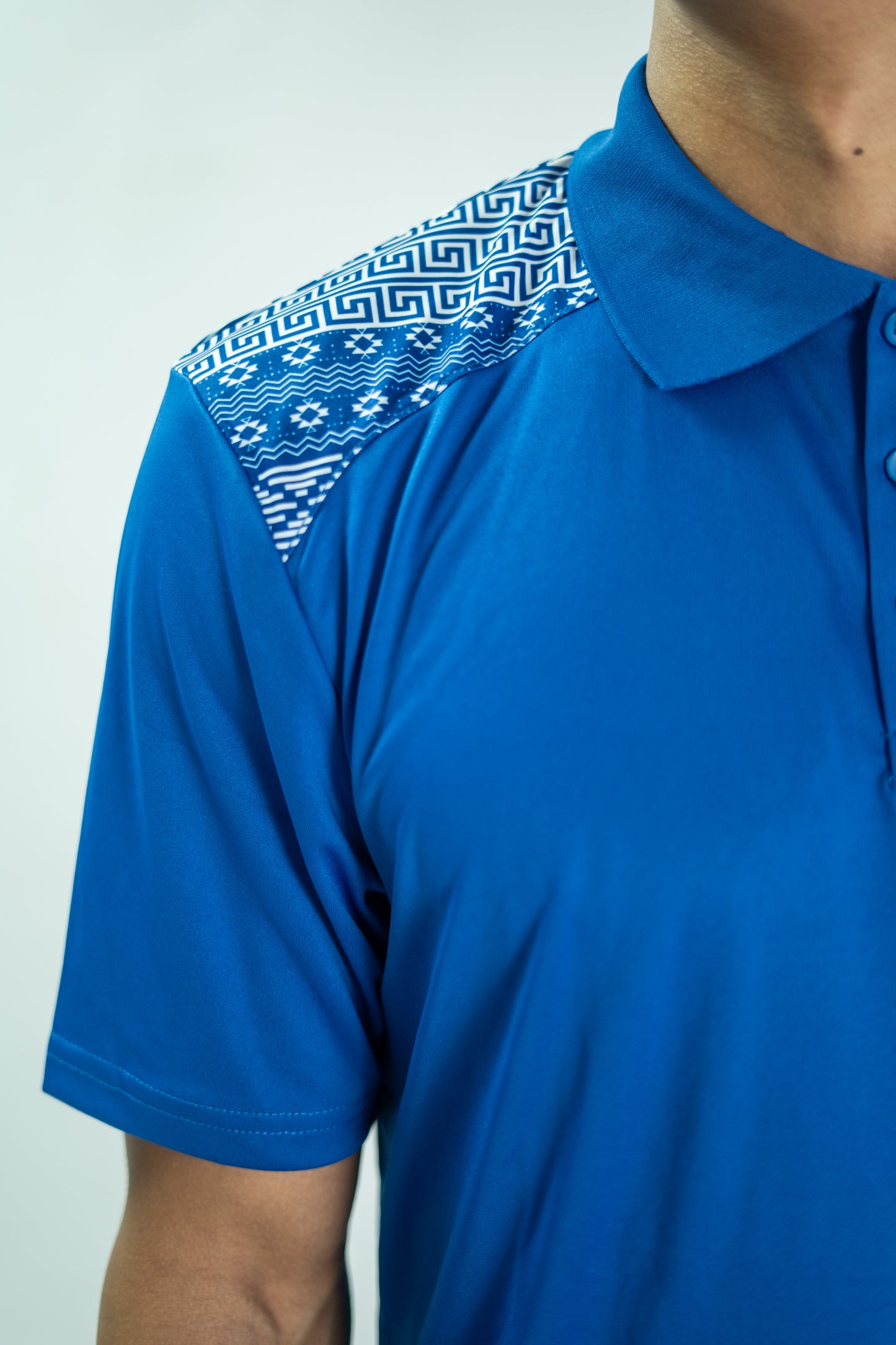 Blue polo shirt with patterned shoulder area on a plain background

