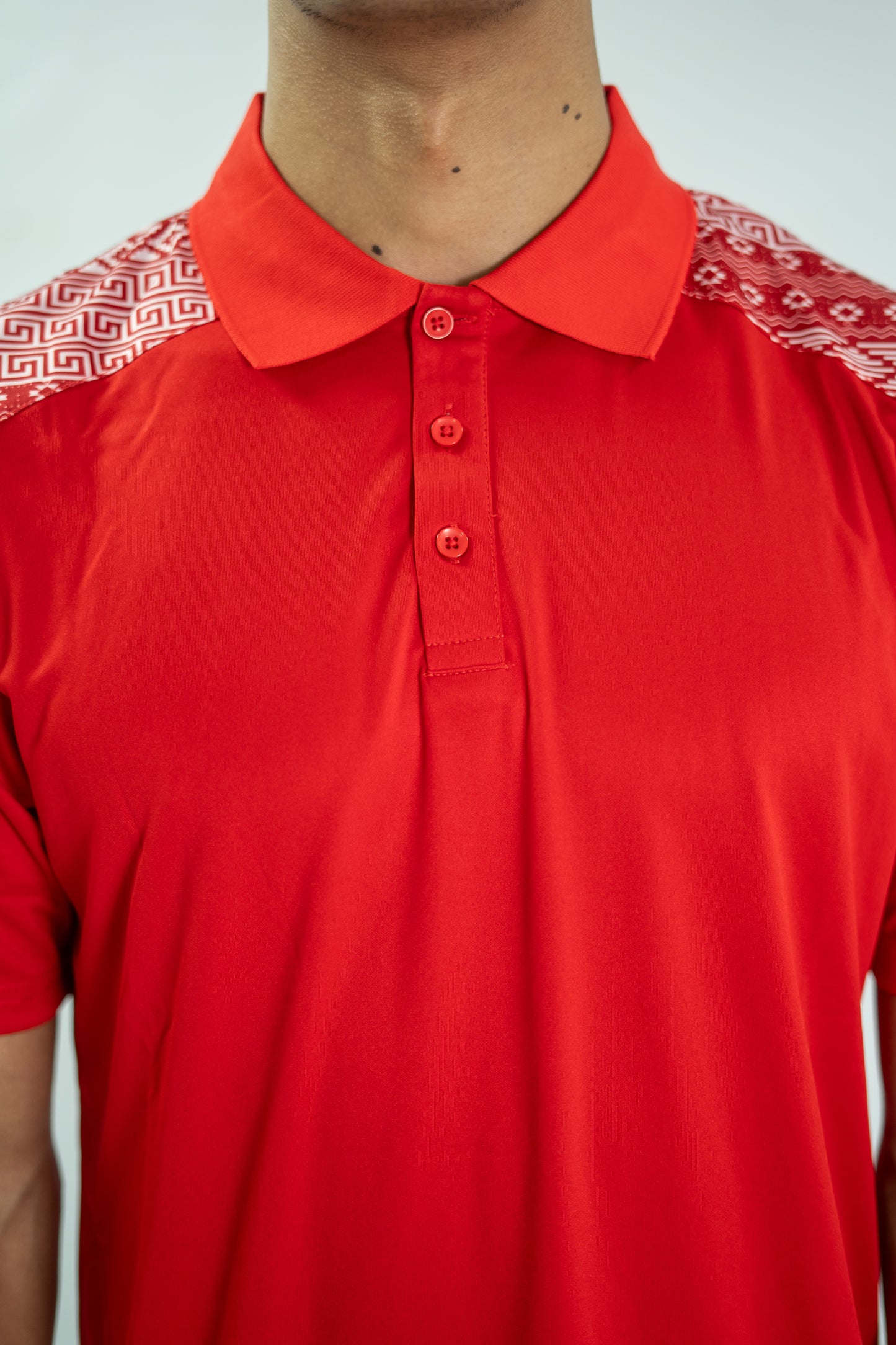 Red polo shirt with patterned shoulders on a plain background


