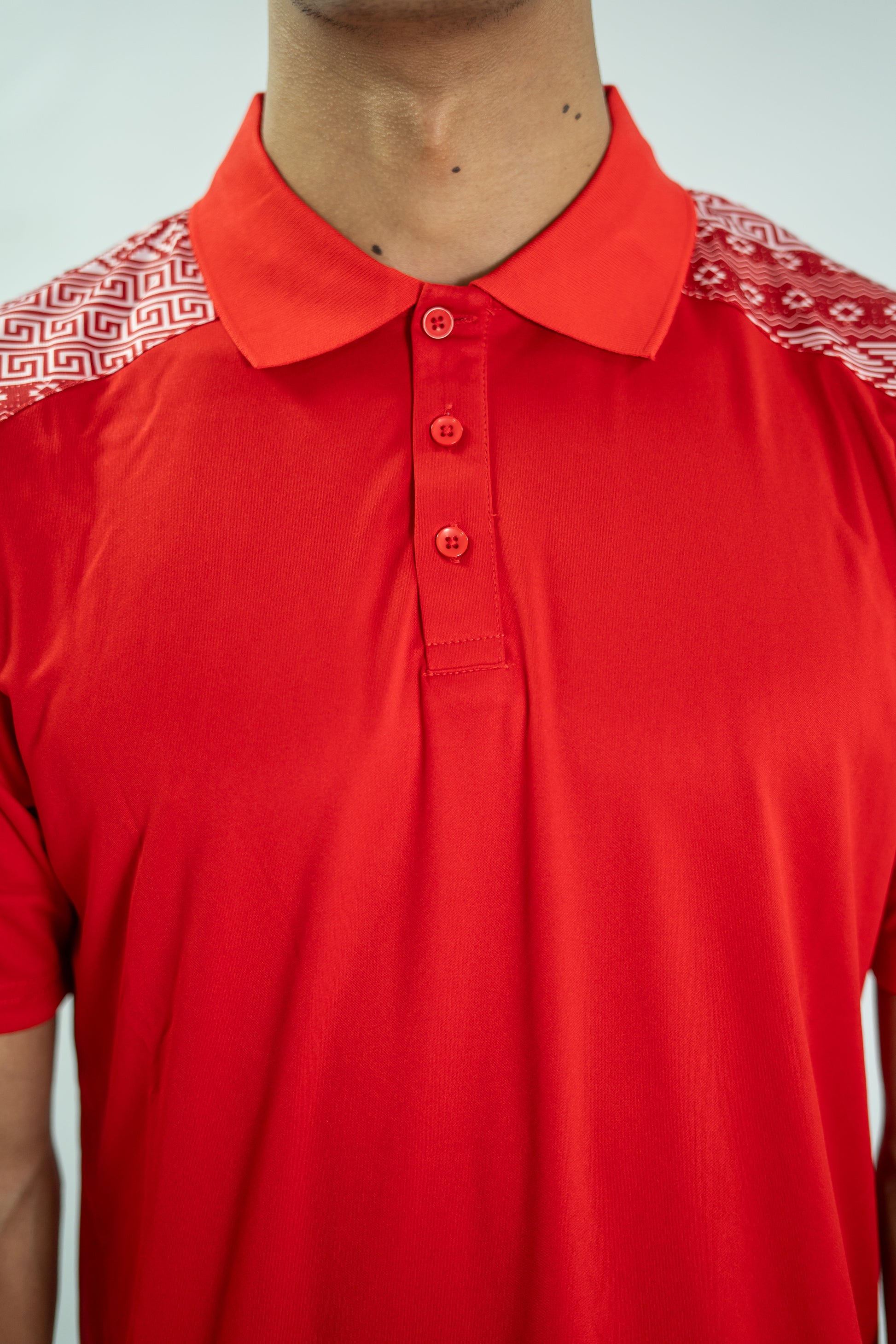 Red polo shirt with patterned shoulders on a plain background

