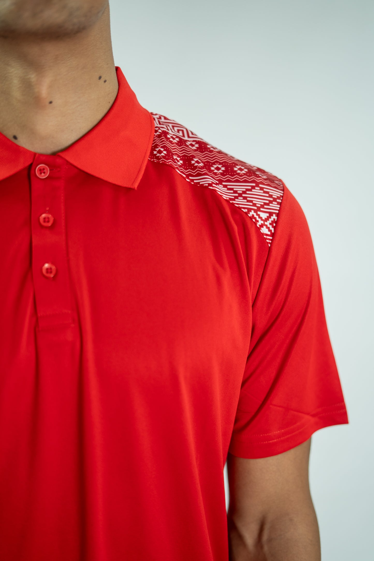 Red polo shirt with white patterned shoulder on a plain background

