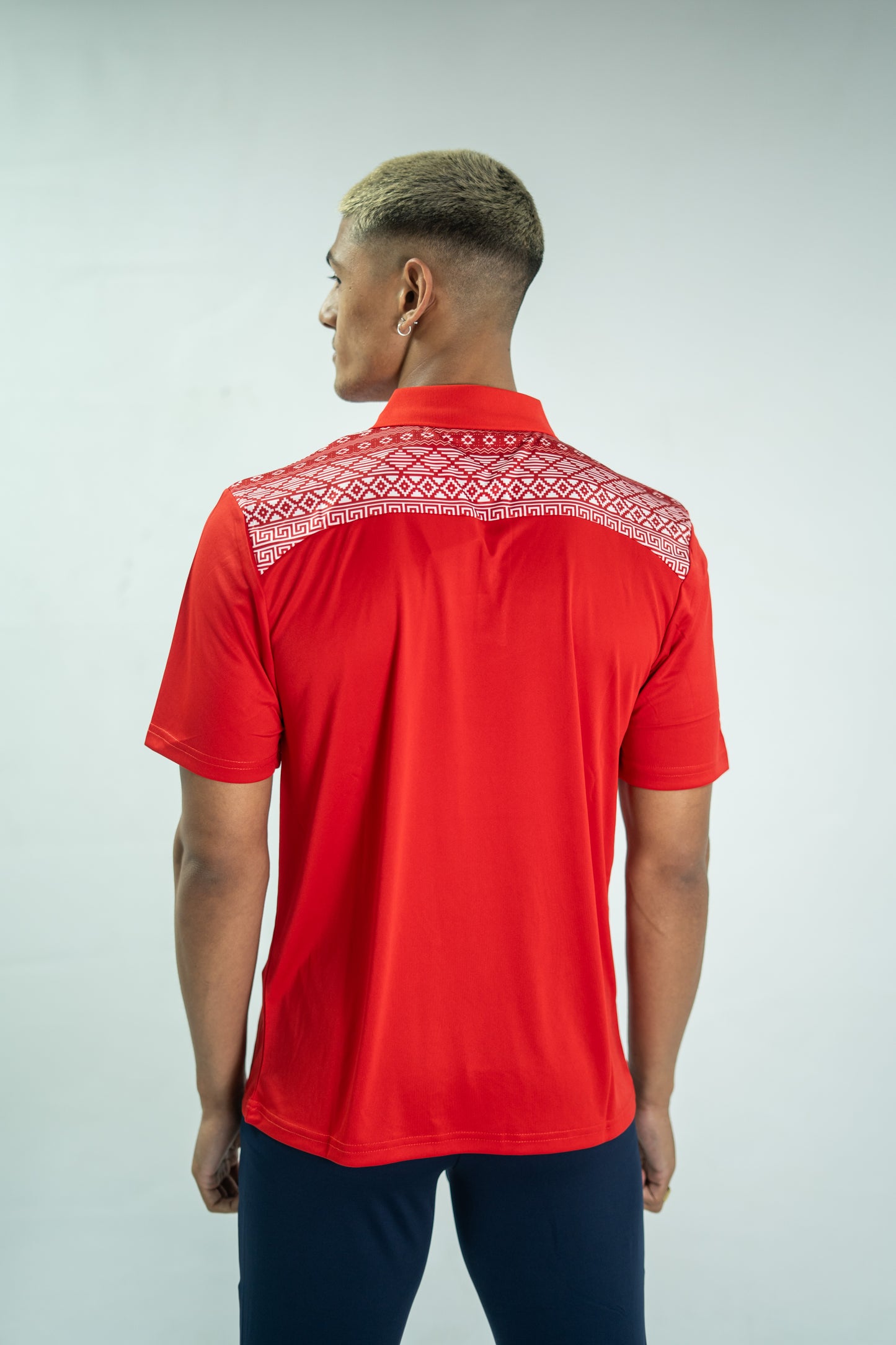 Person wearing a red polo shirt with white patterns on a plain background

