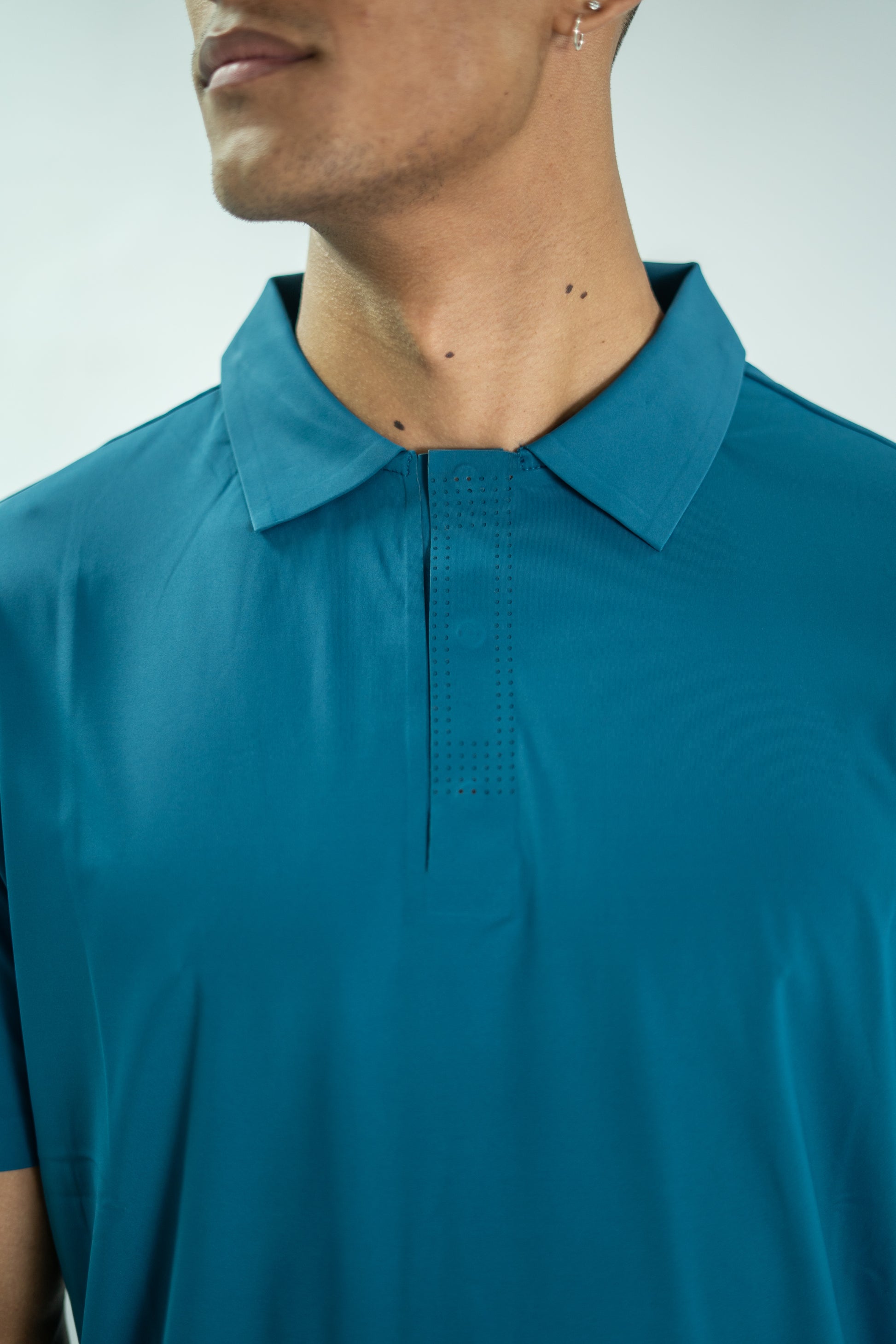 Teal polo shirt worn by a person on a light gray background

