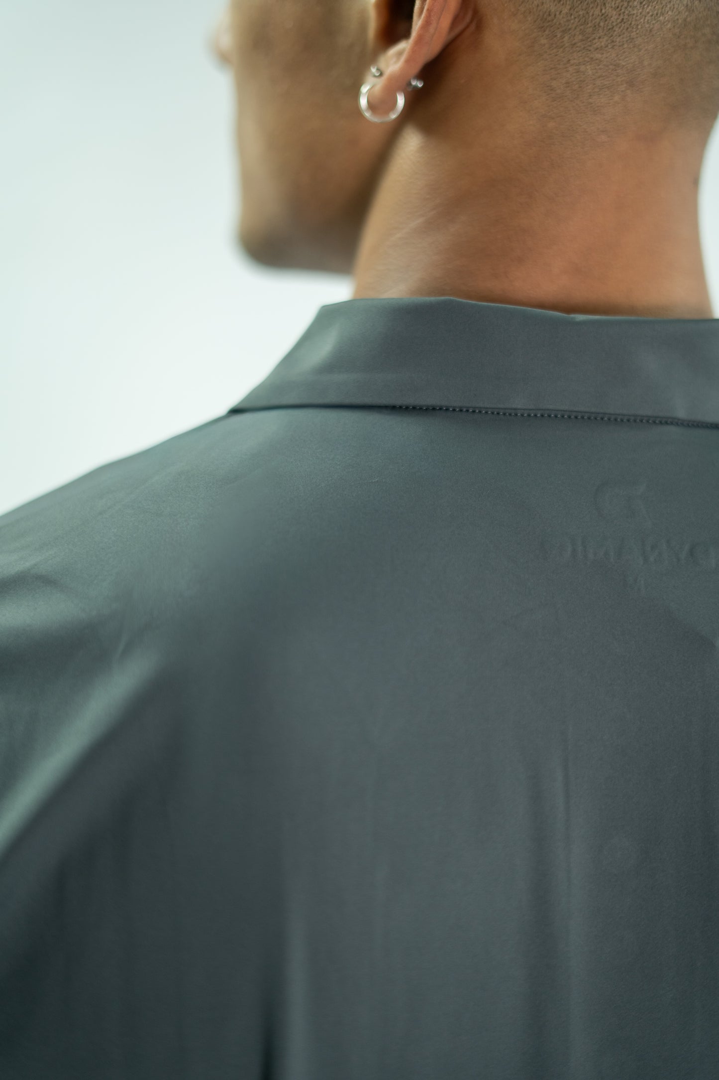 Close-up of a person wearing a dark green shirt with a brand logo on the collar.

