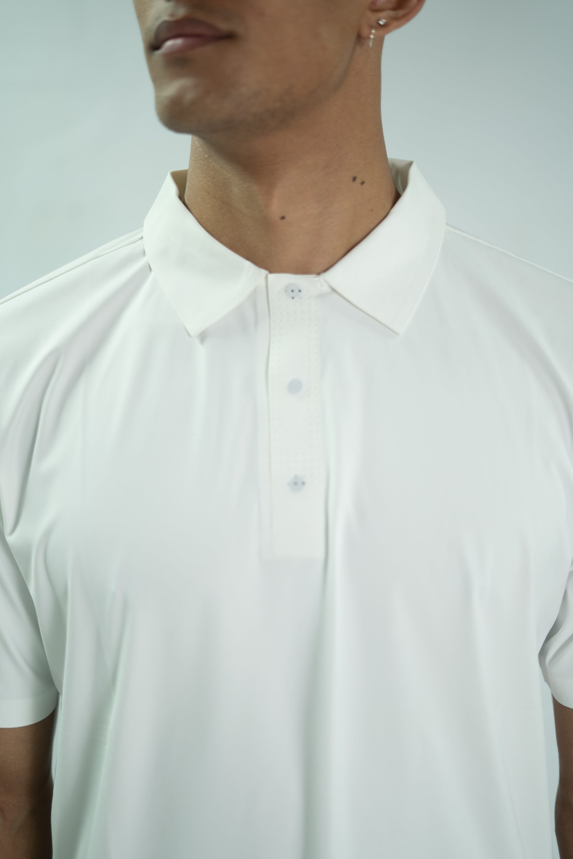 Close-up of a person wearing a white polo shirt against a light gray background

