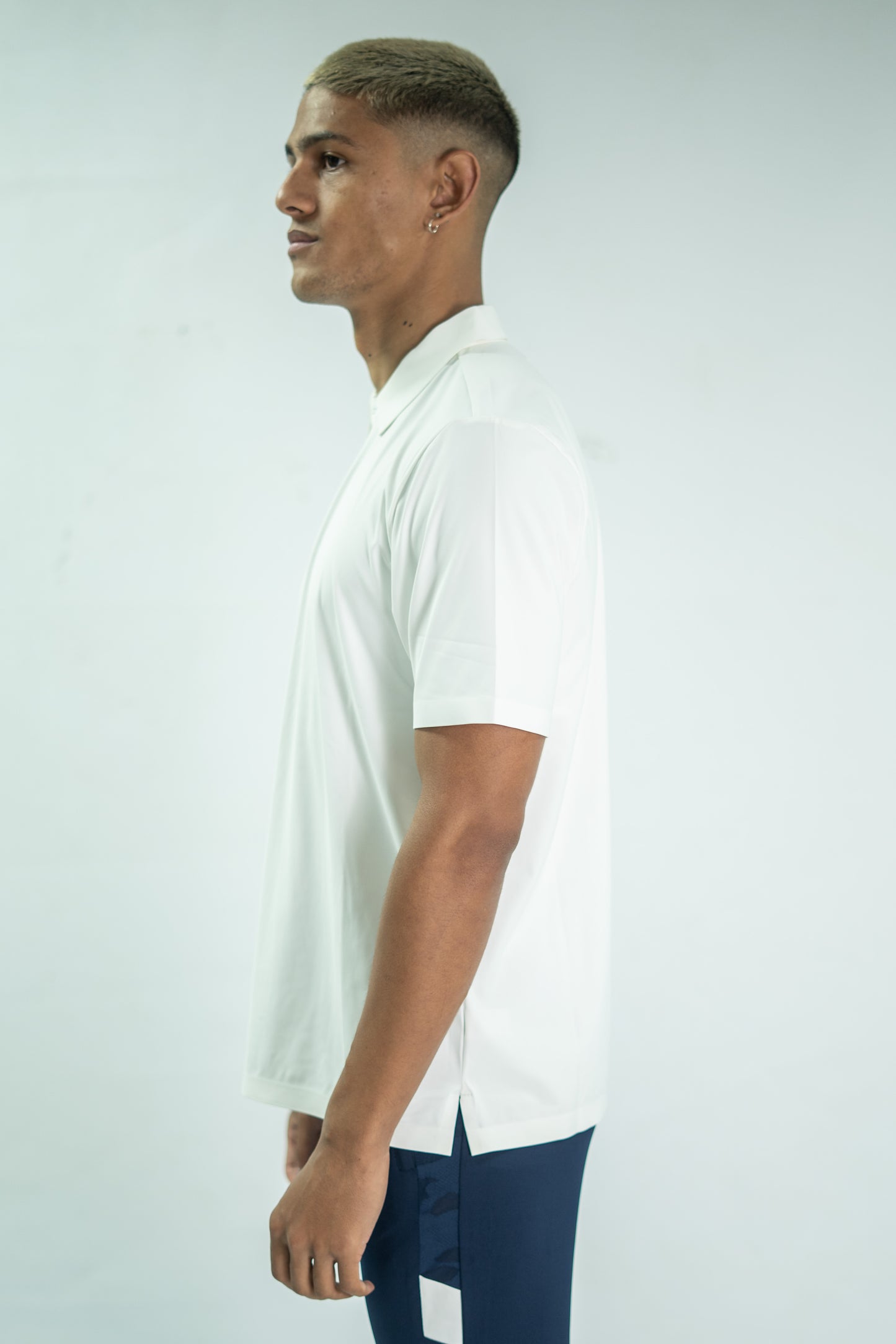 Man wearing a white polo shirt and dark pants on a light gray background

