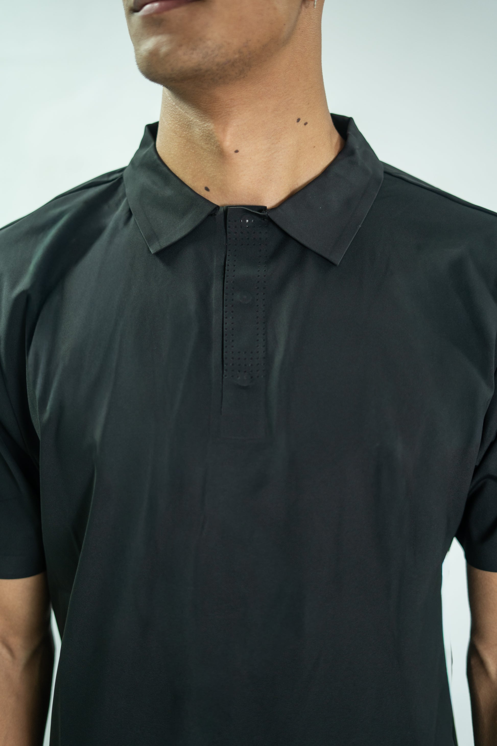 Person wearing a black polo shirt against a plain background

