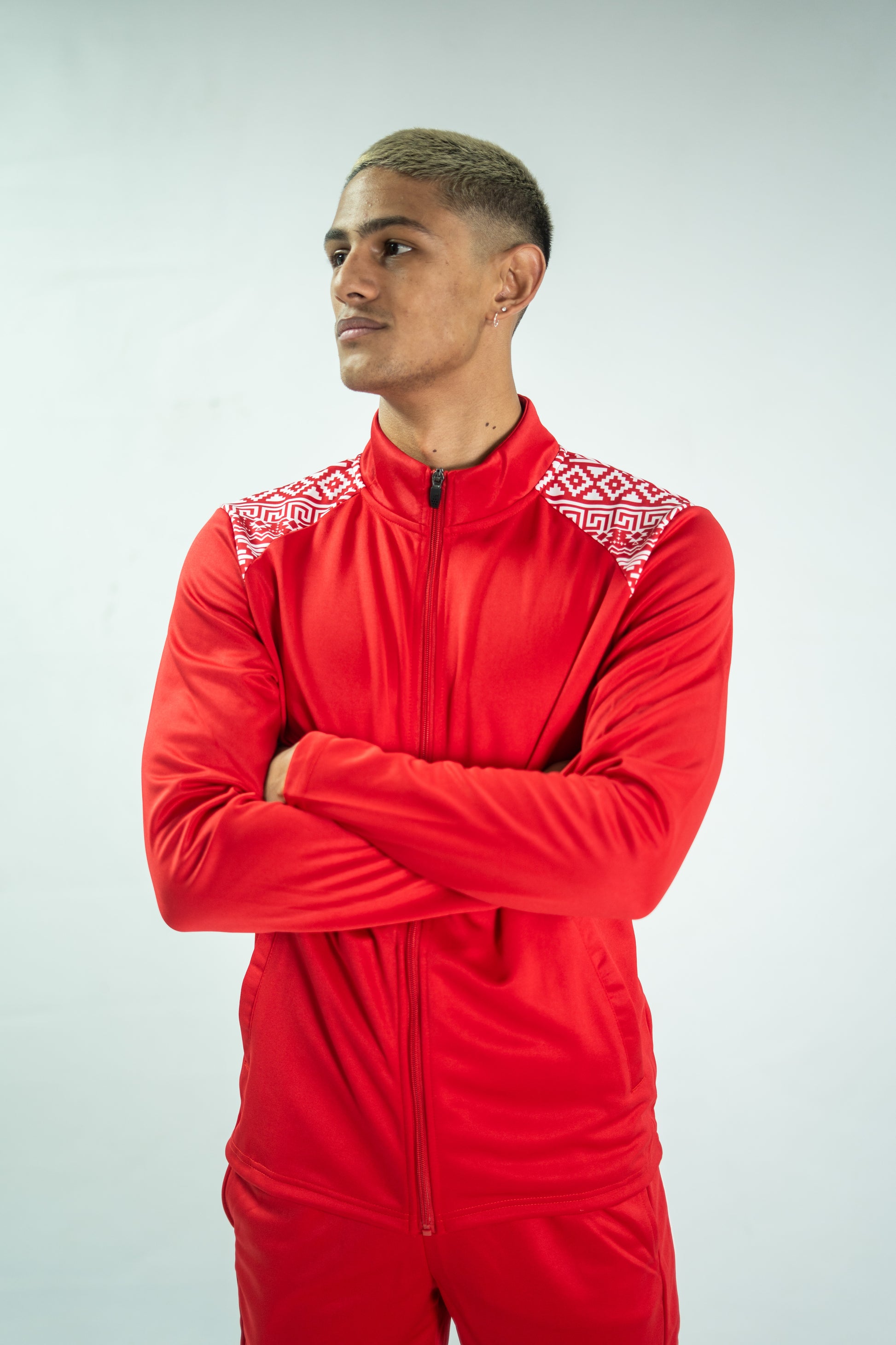 Man wearing a red tracksuit with white patterns on a light gray background

