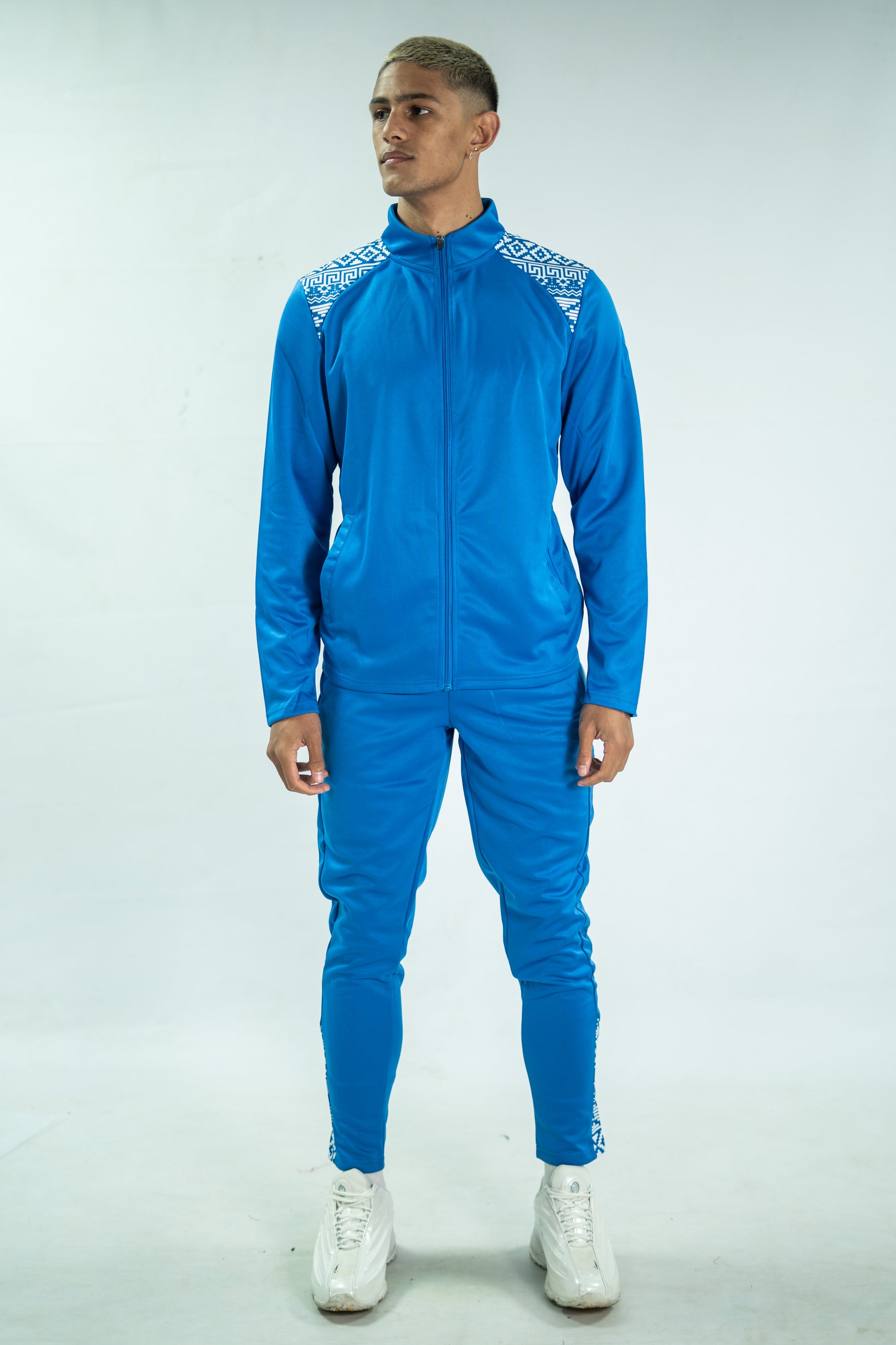 Person wearing a blue tracksuit with white patterns on a light gray background

