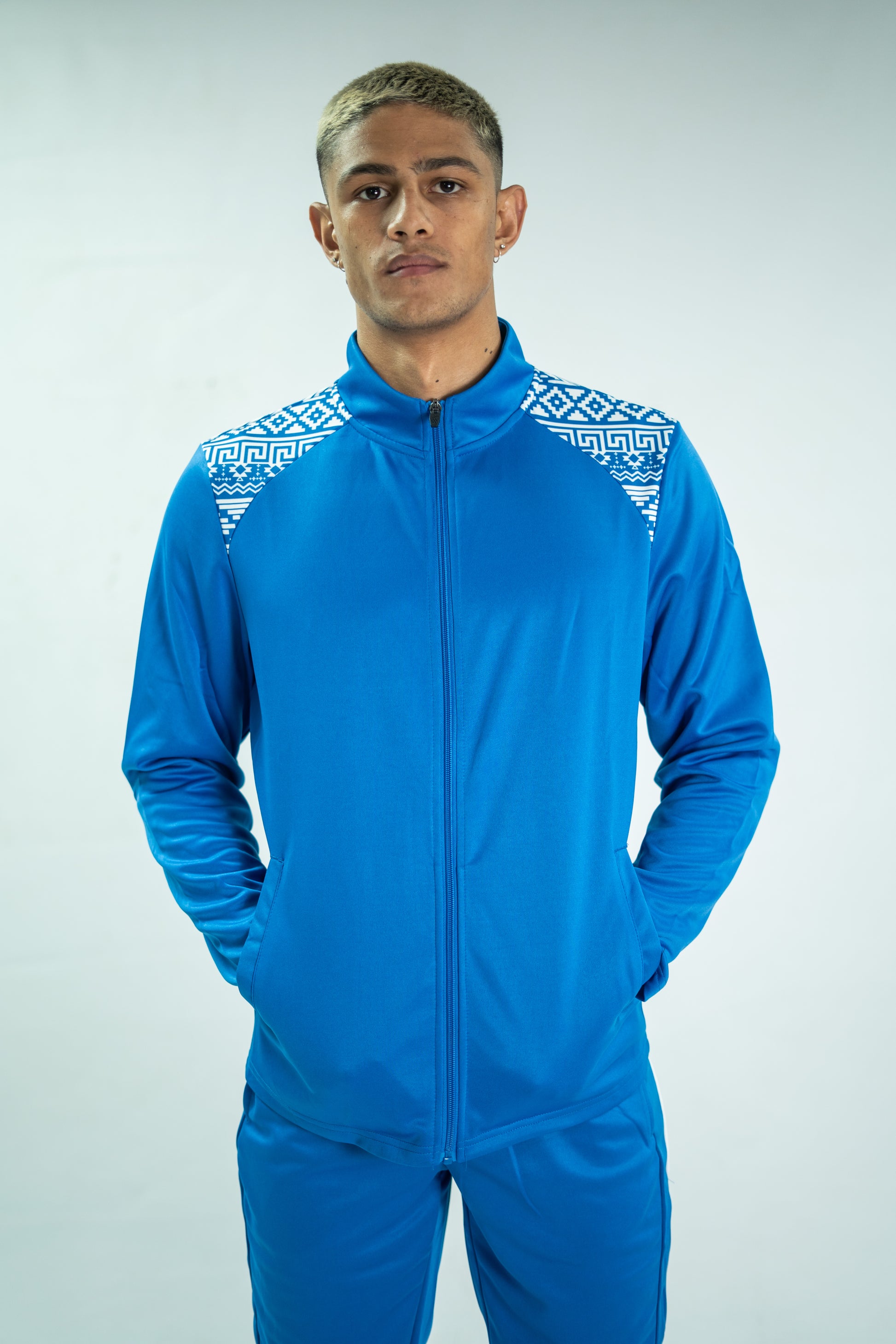 Person wearing a blue tracksuit with white patterns on a light gray background

