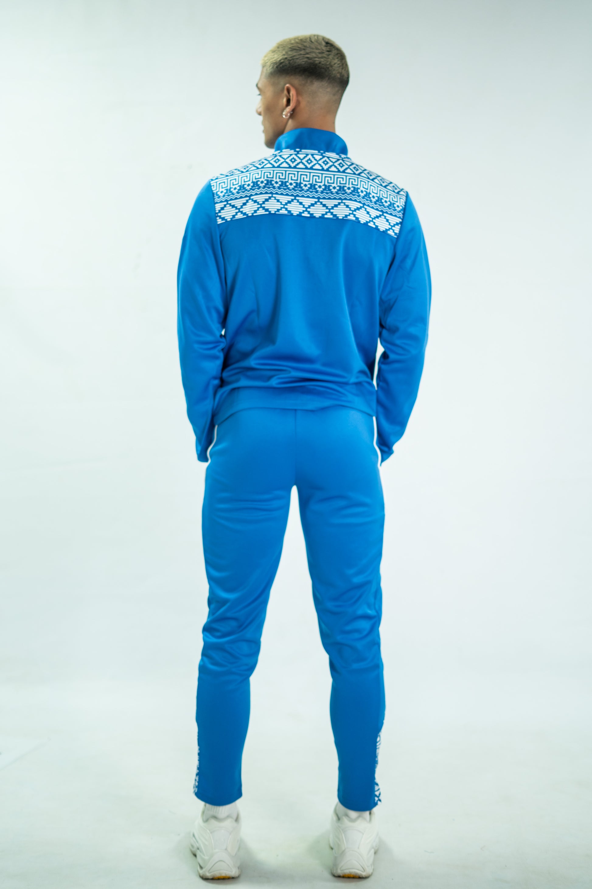 Person wearing a blue tracksuit with white patterns on a light gray background

