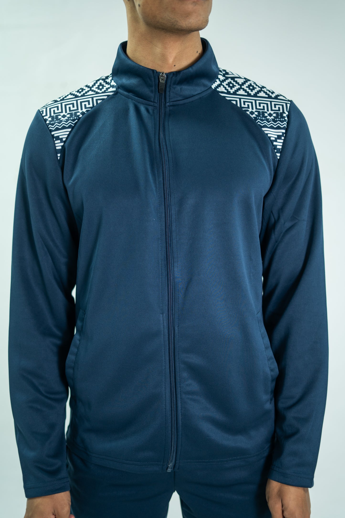 Person wearing a blue tracksuit with patterned shoulders on a light gray background

