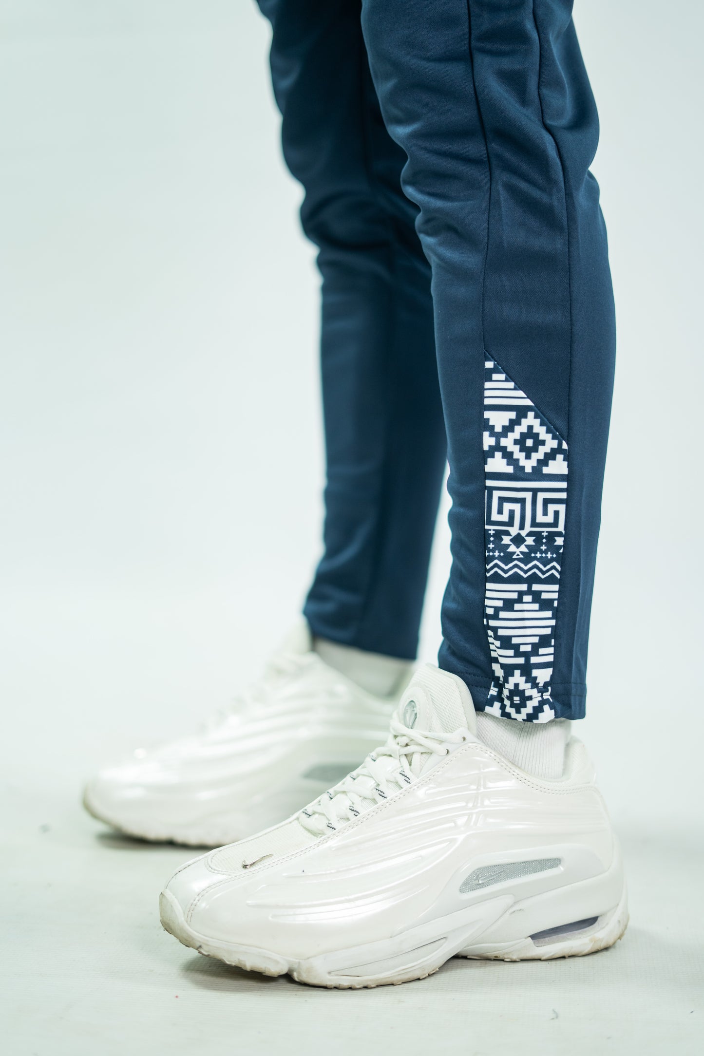 White sneakers with a person wearing blue pants with a geometric pattern on a light gray background

