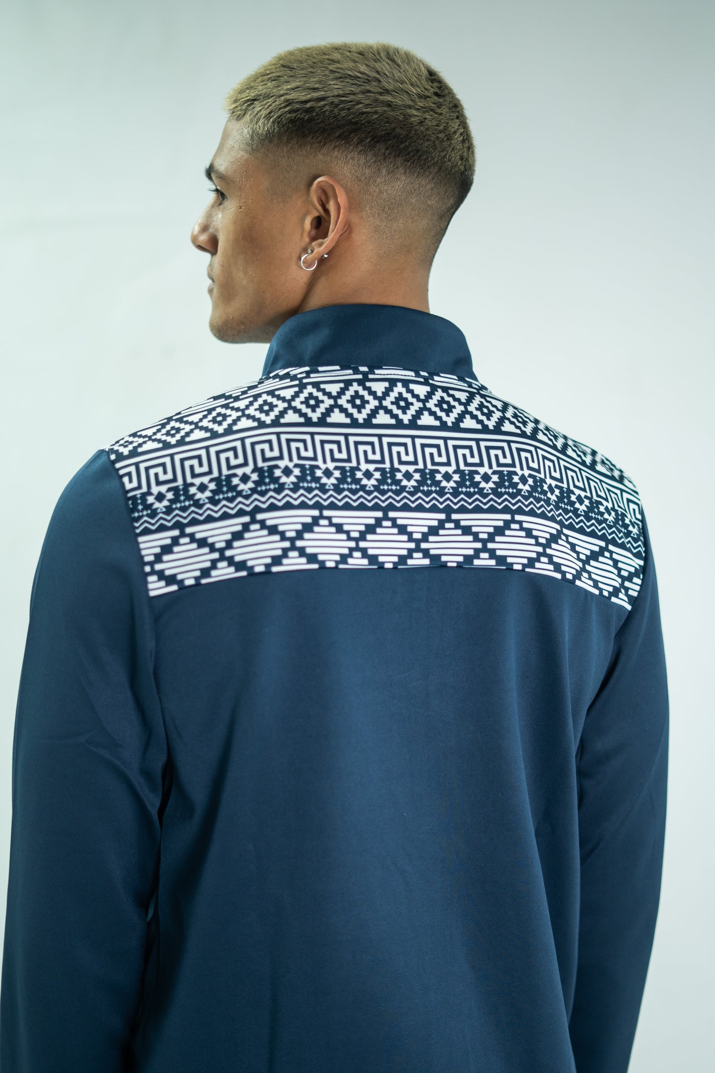 Person wearing a navy blue shirt with a white geometric pattern on the back against a light gray background

