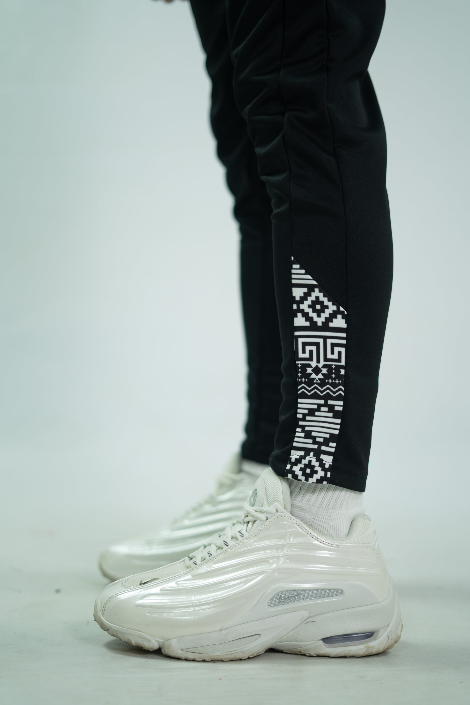 Black pants with geometric pattern and white sneakers on a light gray background

