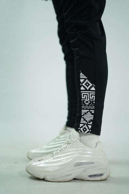 Black pants with geometric pattern and white sneakers on a light gray background

