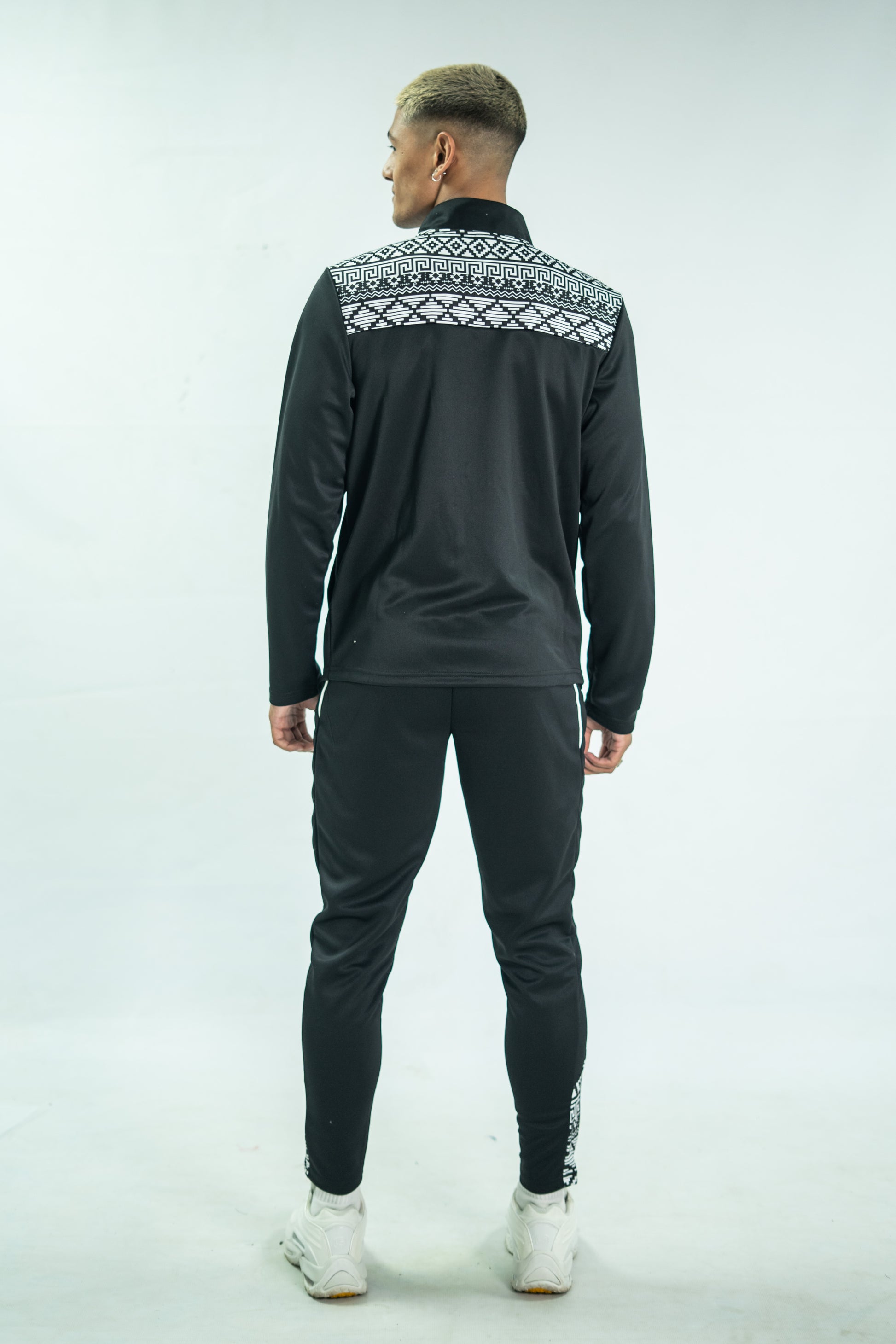 Person wearing a black tracksuit with a patterned chest area on a white background


