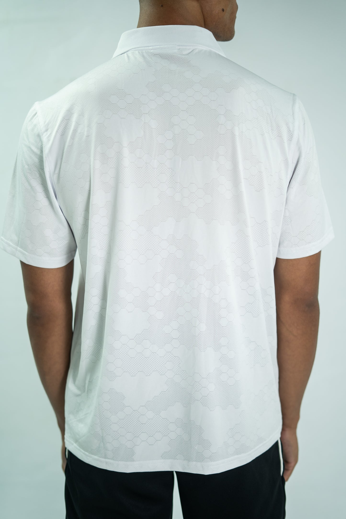 Person wearing a white polo shirt against a light gray background

