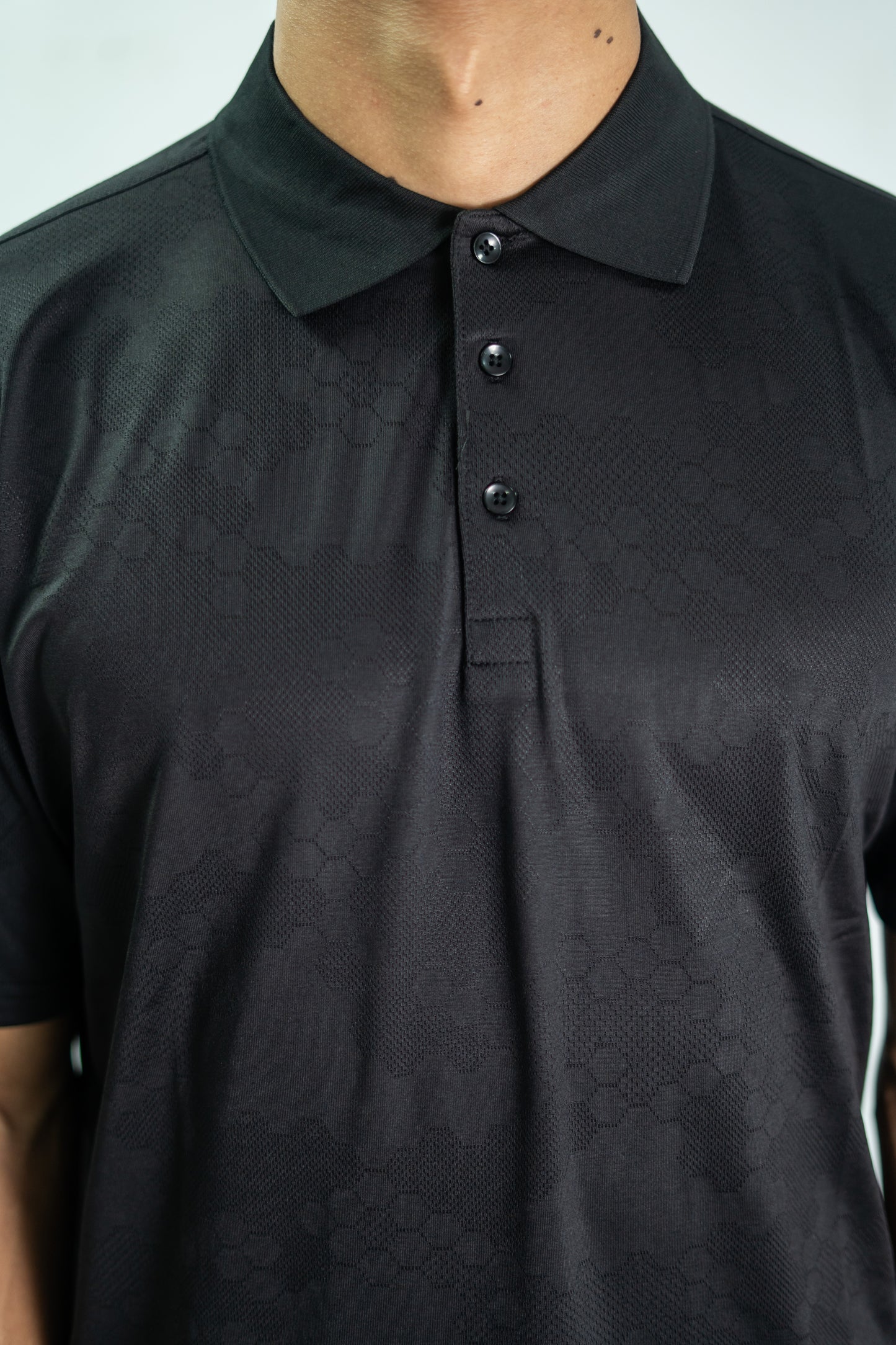 Black textured polo shirt worn by a person on a light gray background

