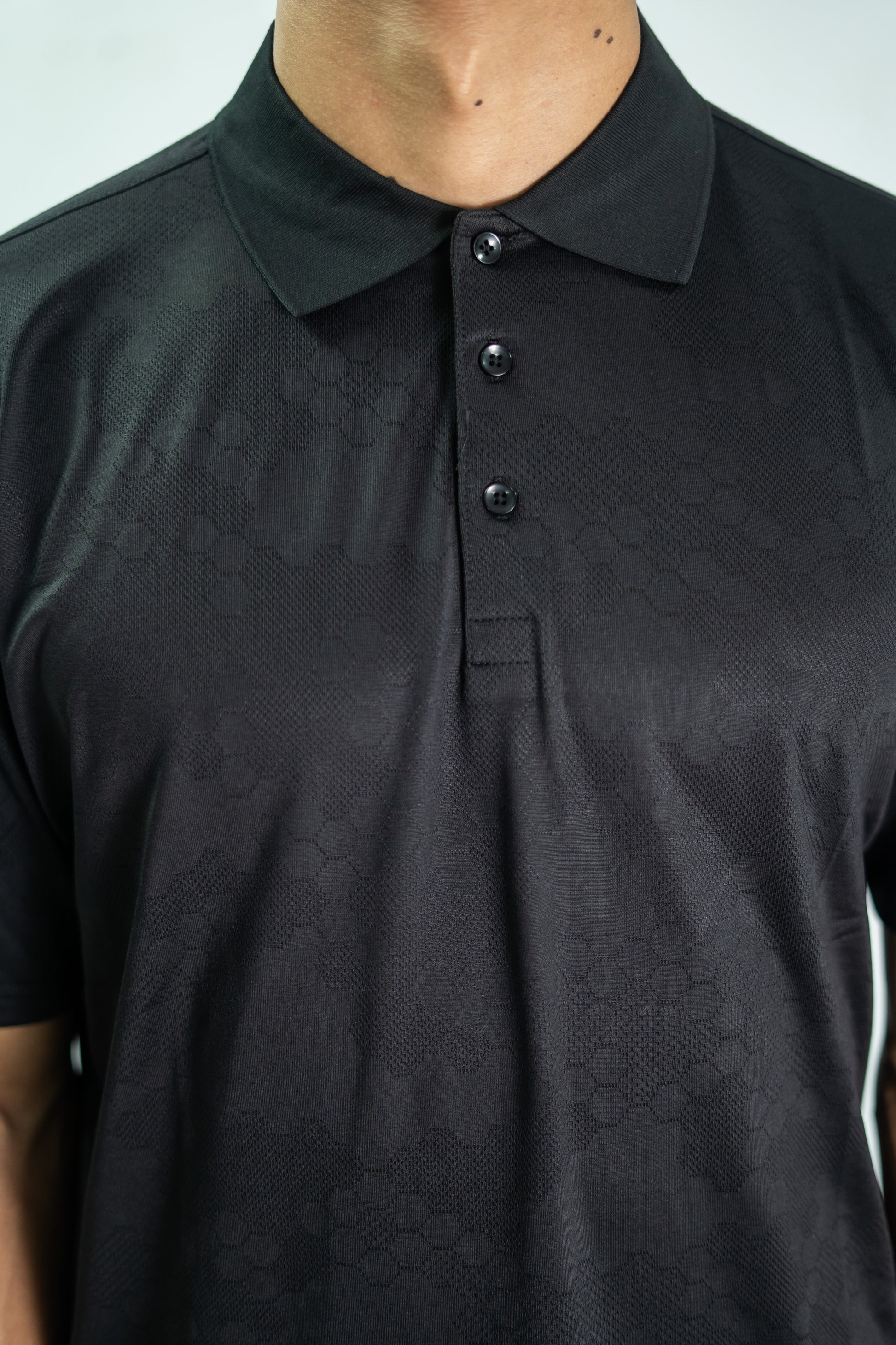 Black textured polo shirt worn by a person on a light gray background

