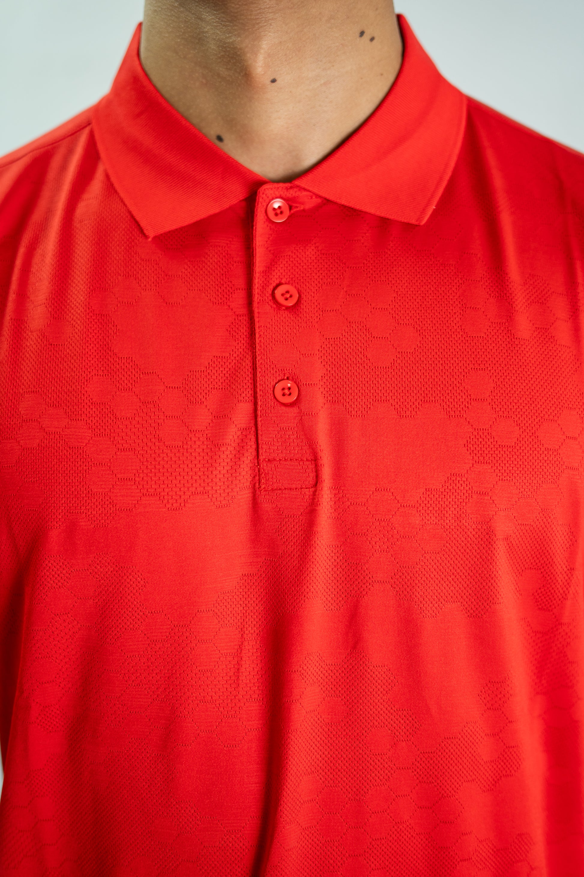 Close-up of a red textured polo shirt with buttons on a light gray background

