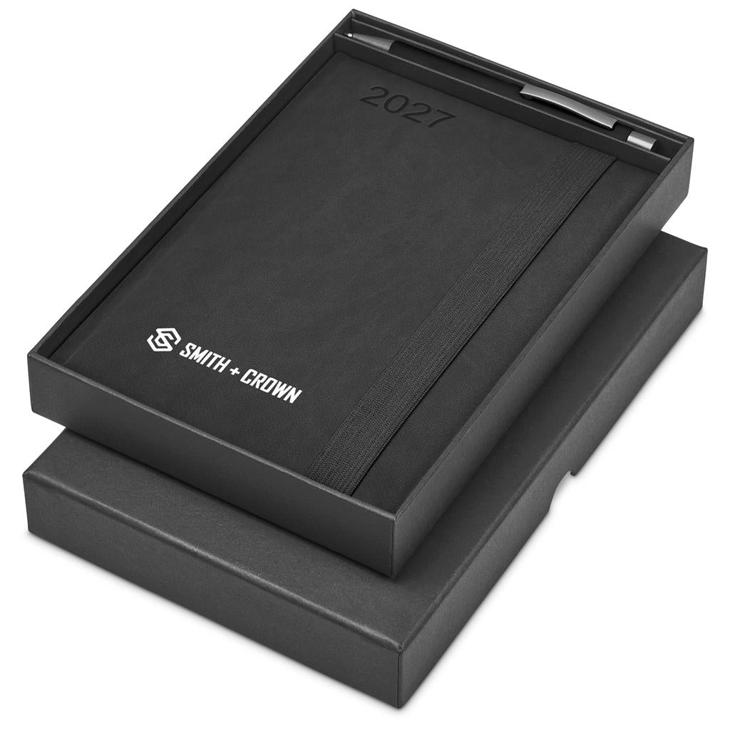 A black Smith + Crown 2027 calendar inside its open presentation box, with the brand logo and '2027' printed on the cover, set against a plain white background.

