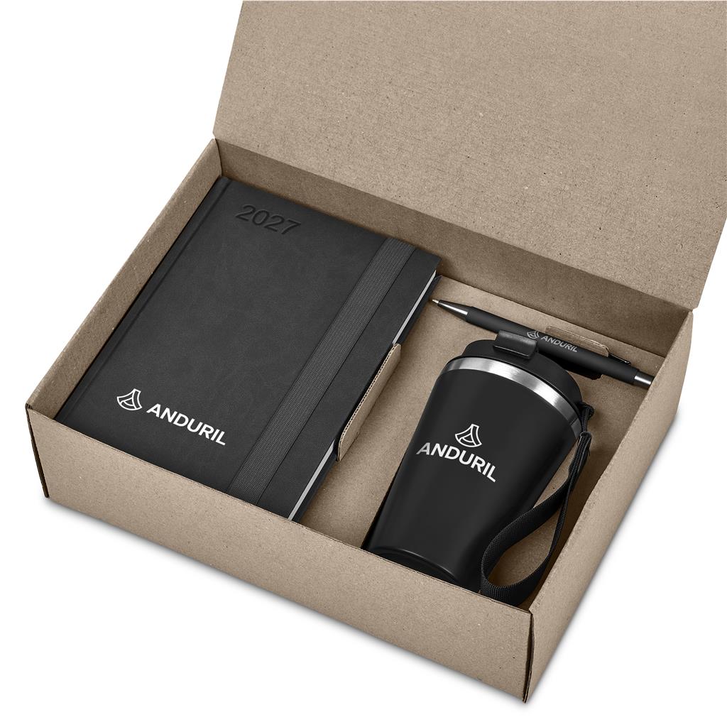 A black branded gift set inside an open kraft cardboard box, including a 2027 notebook, a black insulated tumbler with a pen, and a matching black pouch, all printed with the ANDURIL logo.

