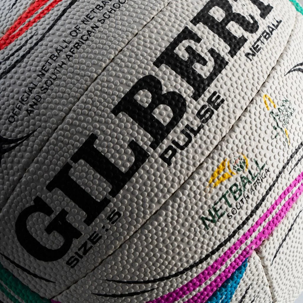 Close-up of a textured Gilbert netball ball showing the Gilbert brand name in black, with size 5 markings and South African Schools netball logos.

